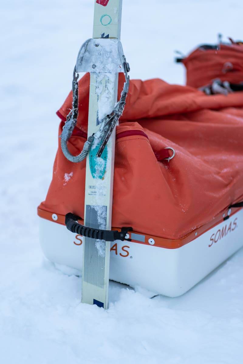 Tukevat kantokahvat helpottavat täyden ahkion nostelua kohteeseen matkustettaessa. Tuulisessa avotunturissa tyhjän ahkion saa ankkuroitua hankeen tökkäämällä suksen kantokahvasta läpi ja peitteen putkia voi käyttää vaikka teltan lumikiiloina. Kuva: Sampsa Sulonen.